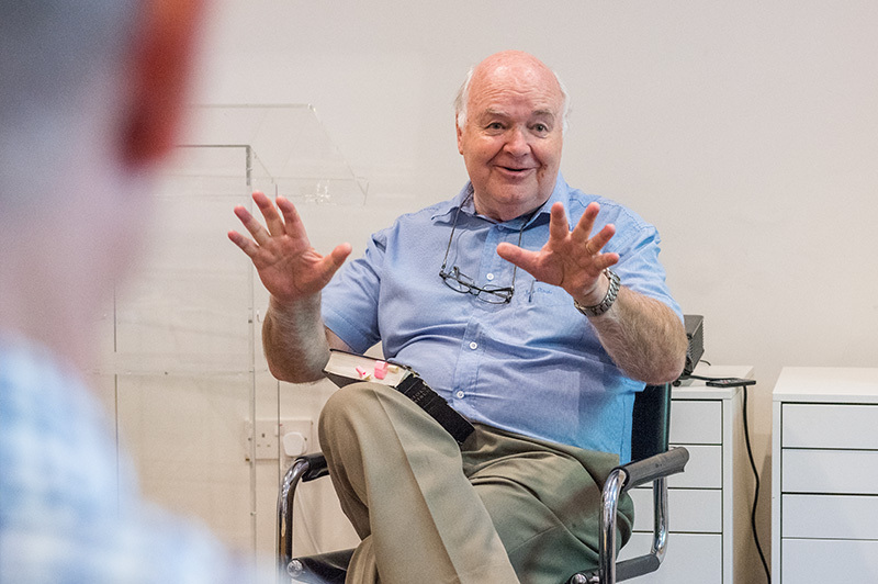Professor Emeritus John Lennox sitting on a chair in a classroom setting speaking